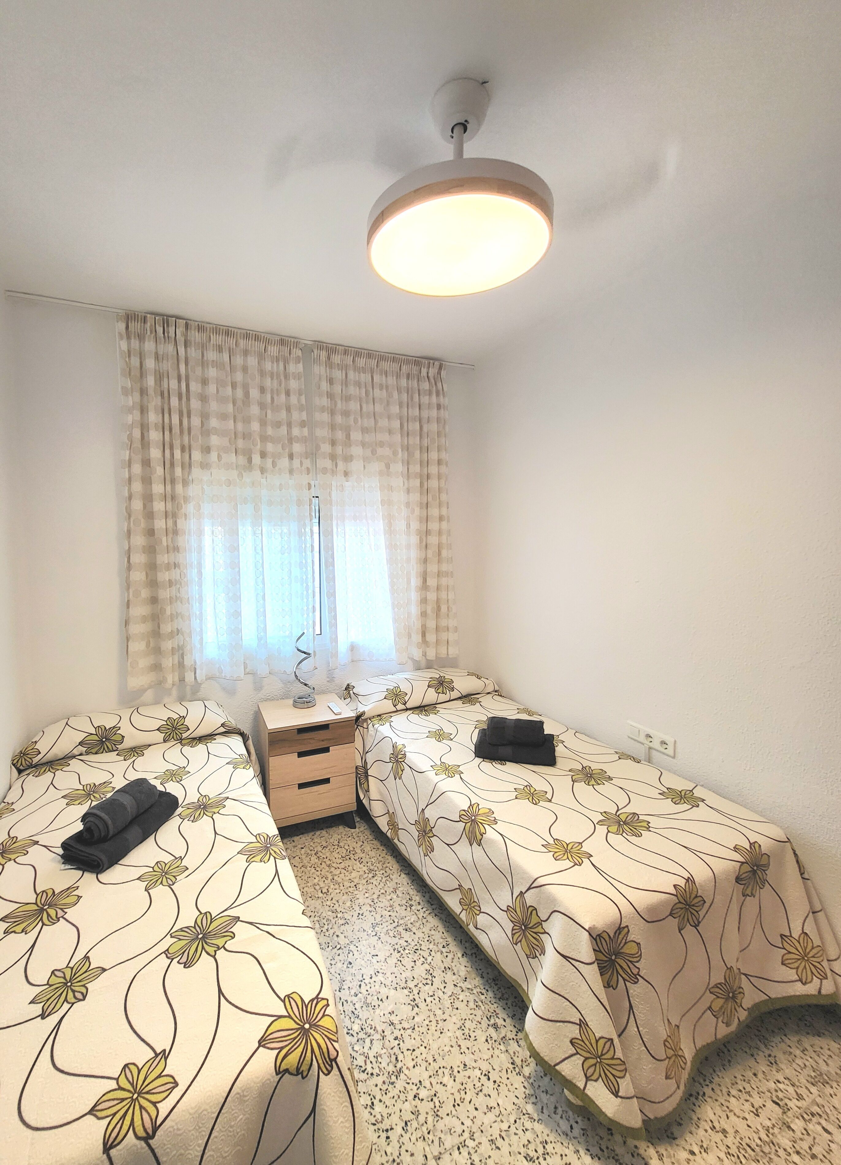 A bedroom with two beds, a desk, a chair, and a ceiling light.