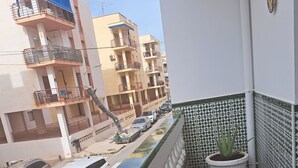 A balcony with a tiled floor, a potted plant, and a view of a street with parked cars and multi-story buildings. - TOWNHOUSE WITH PATIOS, BBQ, FREE WIFI AND PARKING AT 5 'ON FOOT OF THE BEACH (Nerja)