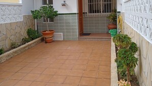A courtyard with tiled flooring, potted plants, a wooden pergola, and a white wall with decorative tiles. - TOWNHOUSE WITH PATIOS, BBQ, FREE WIFI AND PARKING AT 5 'ON FOOT OF THE BEACH (Nerja)