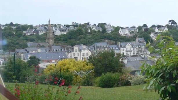 Une vue d’une ville avec une tour imposante, une végétation luxuriante et une chaise au premier plan.