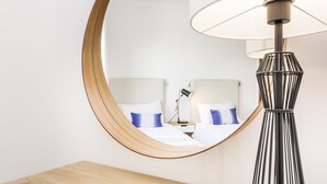 A modern hotel room with a large round mirror, a bed with white and blue bedding, a bedside lamp, and a wooden nightstand. - This is Sea View !!! (Almancil)