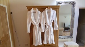 Une armoire en bois sur laquelle sont suspendues deux robes blanches, un miroir avec un cadre orné et un petit banc blanc.