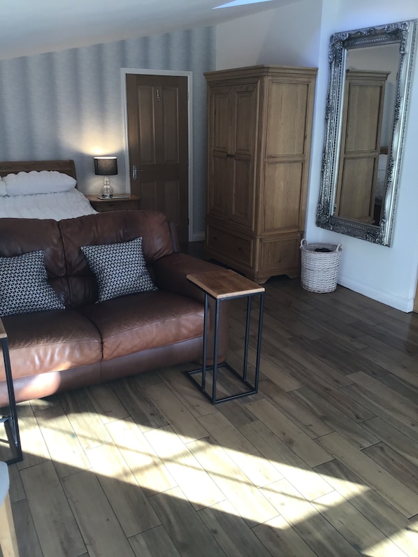 Una habitación con un sofá de cuero marrón, una mesita auxiliar, un armario de madera y un espejo grande en la pared.