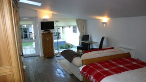 Une chambre à coucher comprenant un lit, une commode, un téléviseur et donnant sur l’extérieur.