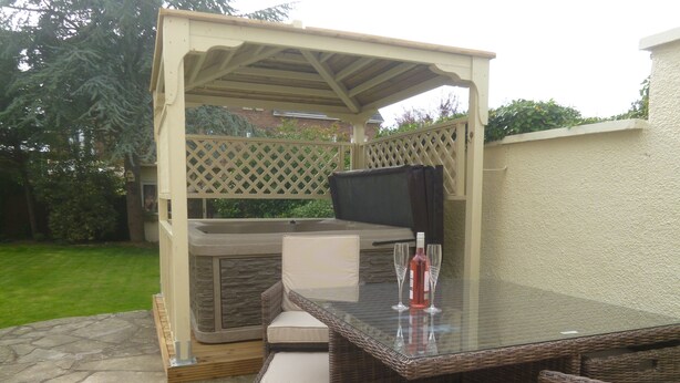 Une terrasse extérieure dotée d’une table à plateau en verre, de chaises en osier, d’un jacuzzi et d’une pergola.