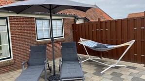 A patio with two lounge chairs and a hammock under a large umbrella.