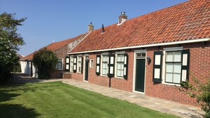 A brick building with a red-tiled roof, a green door, and multiple windows with shutters.
