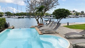 A swimming pool with a wooden deck, lounge chairs, and a view of boats in the background. - Exceptional villa with private sea access private swimming pool central position (GOSIER)