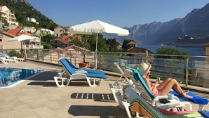 A poolside area with lounge chairs and umbrellas, overlooking a mountainous landscape. - Ground Floor. Private Terrace, Shared Pool, Views across Fjord to Kotor Old Town (Kotor)