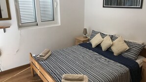 A bedroom with a bed, bedside tables, a lamp, a window with blinds, a framed picture on the wall, and a wooden floor. - Ground Floor. Private Terrace, Shared Pool, Views across Fjord to Kotor Old Town (Kotor)
