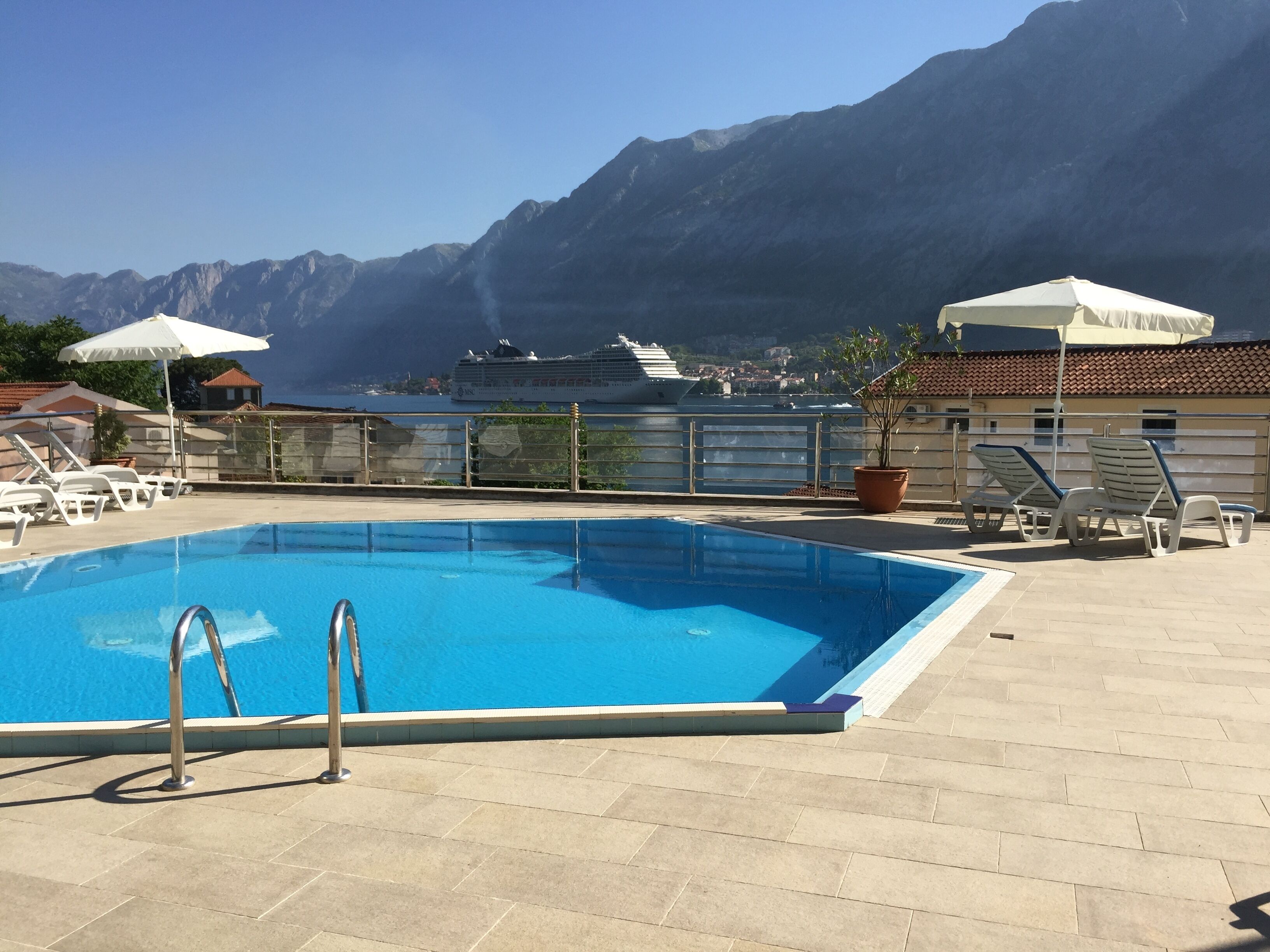 A swimming pool with a view of mountains and a cruise ship in the background.