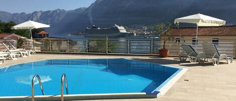 A swimming pool with a view of mountains and a cruise ship in the background.