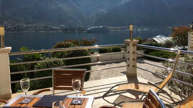 An outdoor terrace with a table and chairs, overlooking a lake and mountains. - Ground Floor. Private Terrace, Shared Pool, Views across Fjord to Kotor Old Town (Kotor)