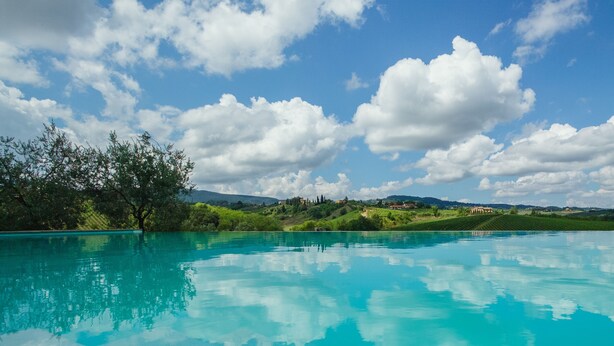 Piscina cristallina con vista su dolci colline verdi e un cielo parzialmente nuvoloso.