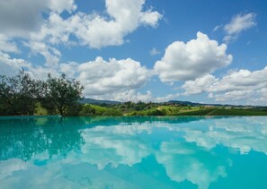 A clear blue pool with a view of green hills and a partly cloudy sky.
