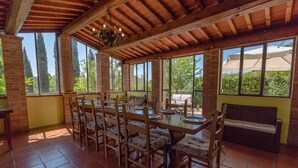 Zona pranzo con tavolo e sedie in legno, ampie finestre e parete in mattoni.