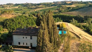 Un edificio bianco con tetto in tegole, circondato da alberi e campi.