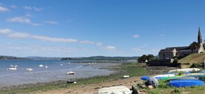 Eine Küstenlandschaft mit Booten am Ufer, einer Kirche und Blick auf das Meer.