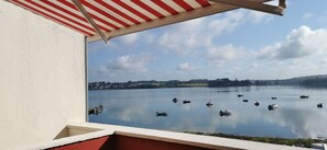Blick auf einen See mit Booten, ein rot-weiß gestreifter Sonnenschirm und ein klarer Himmel.