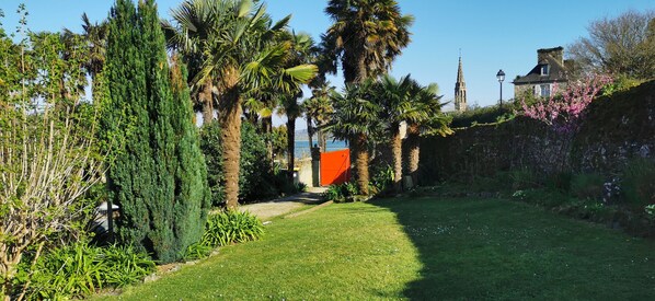 Een verzorgde tuin met palmbomen, een stenen muur en een uitzicht op een historisch gebouw op de achtergrond.