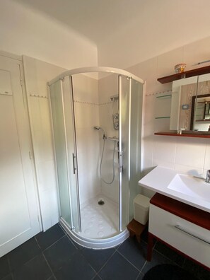 Un baño moderno con ducha envuelta en vidrio, un lavamanos blanco y un mueble de tocador de madera.