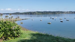 Un port tranquille, avec des bateaux à l’ancre, une rive verdoyante et une ville qui se dessine à l’horizon.