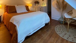 Ein Schlafzimmer mit Dachfenster, einem Bett mit weißer Decke, Holzboden und dekorativen Wandbildern.