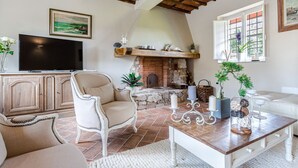 A living room with a fireplace, a television, and a dining area with a table and chairs. - A Romantic Farmhouse with Pool in 10 mins walk away from the Walls of Lucca (Monte San quirico)