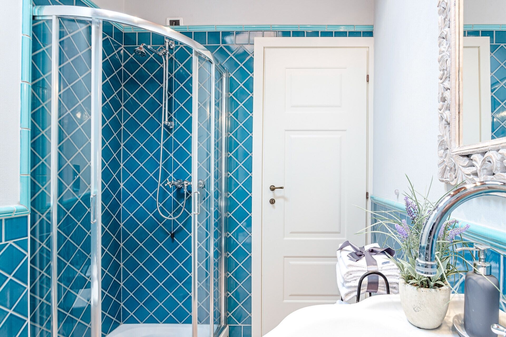 A bathroom with a glass shower enclosure, a white door, and a sink area with a towel and potted plant.