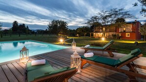 A wooden deck with lounge chairs and a pool, surrounded by a landscaped garden and a house with warm lighting. - A Romantic Farmhouse with Pool in 10 mins walk away from the Walls of Lucca (Monte San quirico)