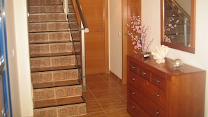 Una escalera con baldosas estampadas, una puerta de madera, un aparador con cajones y un espejo en la pared.