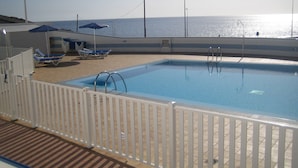 Piscina con cerca blanca, sillas de descanso y sombrillas.