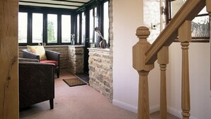 A cozy room with a stone fireplace, a wooden staircase, and a view of the outdoors through large windows. - The Cotswold Manor Hall, Exclusive Hot Tub, Games Barn, 70 acres of Parkland (Bampton)
