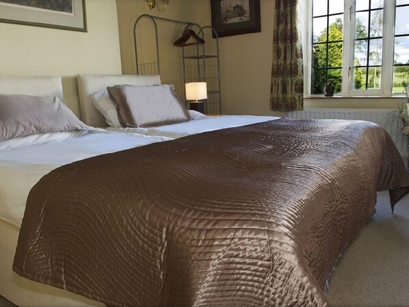 A neatly made bed with a brown cover, a bedside lamp, and a window with a view of greenery.