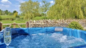 A hot tub with a stone wall and wooden fence in a garden setting. - The Cotswold Manor Hall, Exclusive Hot Tub, Games Barn, 70 acres of Parkland (Bampton)