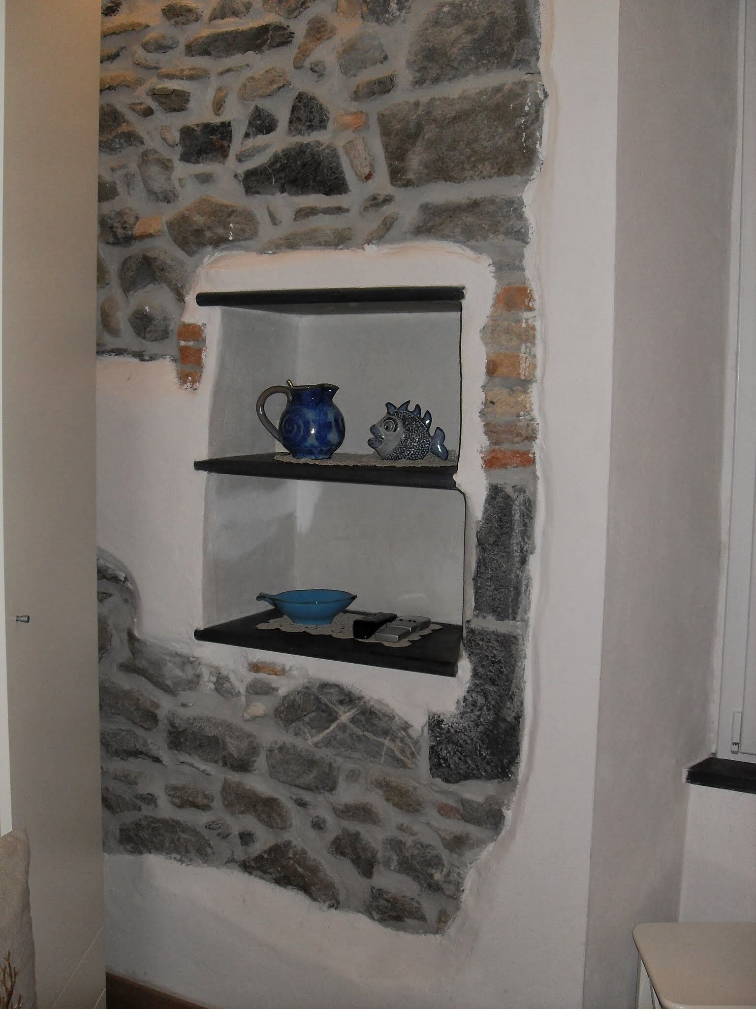 A stone wall with a shelf holding a blue pitcher, a fish-shaped ornament, and a blue bowl.