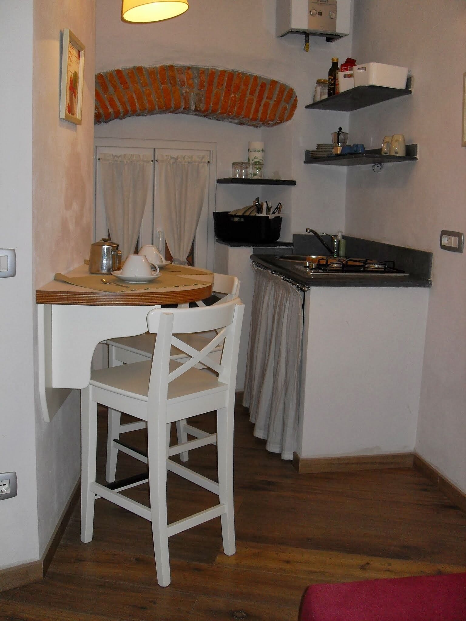 Eine kompakte Küche mit Essbereich, ausgestattet mit einem kleinen Tisch, zwei Stühlen, einem Herd und Regalen mit Küchenutensilien.