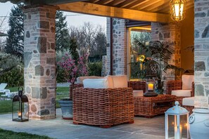 An outdoor patio with wicker furniture, stone pillars, and potted plants.