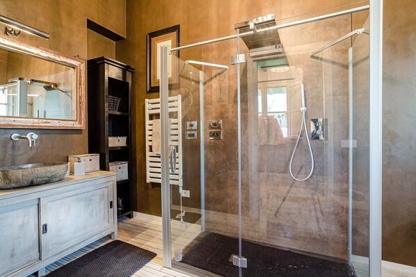A modern bathroom with a glass-enclosed shower, a large mirror, and a wooden vanity.
