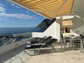 Een balkon met uitzicht op zee en boten, een tafel met stoelen en een gestreept zonnescherm.