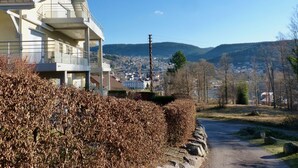 Un edificio moderno con un balcón, vistas despejadas de un pueblo y montañas al fondo, y una carretera que se extiende hasta el horizonte.