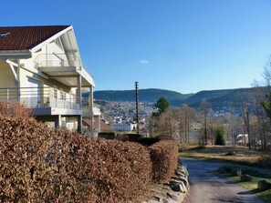 Un bâtiment moderne doté d’un balcon, offrant une vue dégagée sur une ville et des montagnes en arrière-plan, et une route qui s’étend à perte de vue.