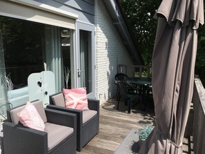 Een terras buiten met rieten meubels, een tafel en stoelen.