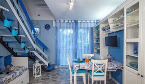 A room with a staircase, a dining area with a table and chairs, and a bookshelf.