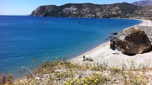 Ein Küstenstrand mit klarem, blauem Wasser, einem Felsen und einem entfernten Gebirgszug.