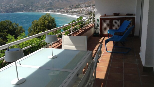 Ein Balkon mit Tisch, Stühlen und Blick auf das Meer und die Berge.