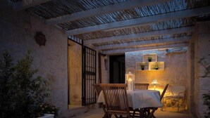 An outdoor dining area with a table and chairs, a stone wall, and a thatched roof.