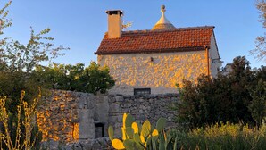 A stone building with a red-tiled roof, surrounded by lush greenery and flowering plants.