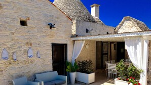 A stone building with a covered patio, wicker furniture, and potted plants.