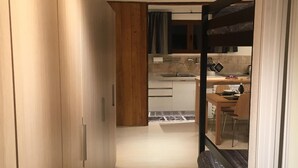 A narrow hallway leading to a kitchen with wooden cabinets, a dining table, and a bench. - Casa Cervinia Apartment  (Breuil Cervinia)